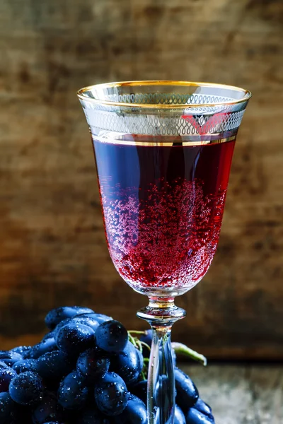 Red sparkling wine in the glass, blue grapes in the wine cellar