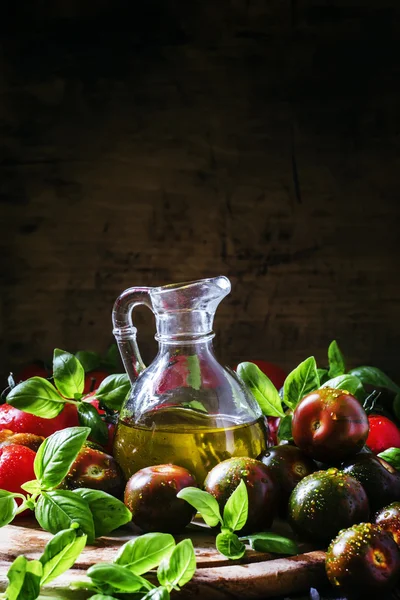 Olive oil in a jug, green basil leaves, black and red tomatoes