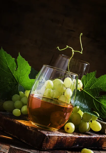 White wine in a glass, green grapes with leaves in a wine cellar