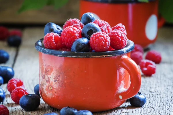 Fresh raspberries and blueberries in red enamel mug