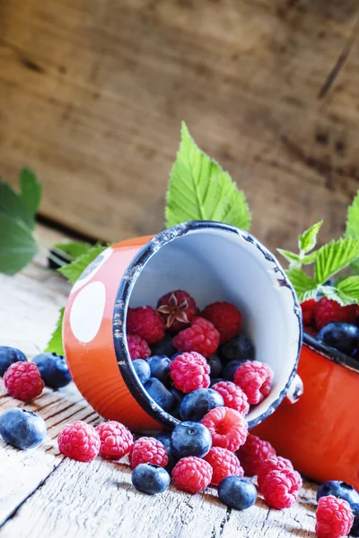 Raspberries and blueberries in red enamel mugs