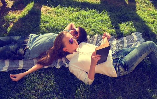 Little teenage boy and girl are lying on grass, girl reads book and boy wears earphones chillout