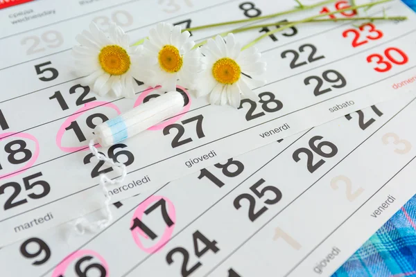 White calendar with pink circles around menstruation date period and clean tampons lying on top.