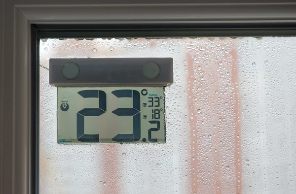 Street thermometer behind window in rainy weather