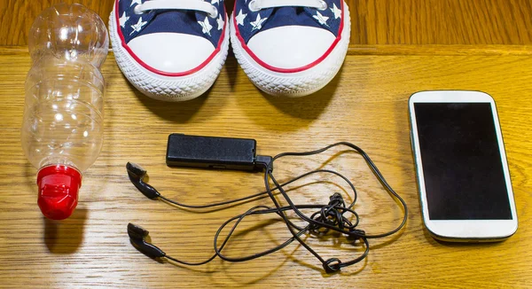 Sport shoes, water, earphone and phone on wooden background