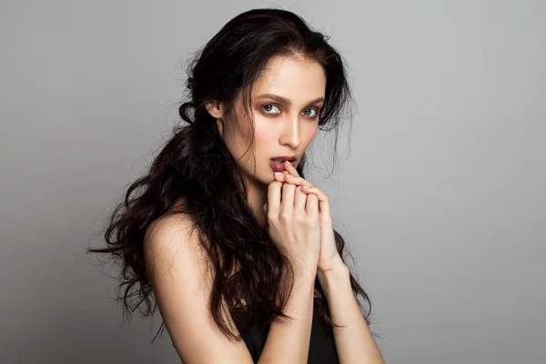 Beautiful face of young adult woman with long fluffy hair on gray background with hands around lips.