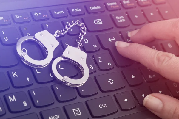Cybercrime concept with small handcuffs on computer keyboard and police lights illumination