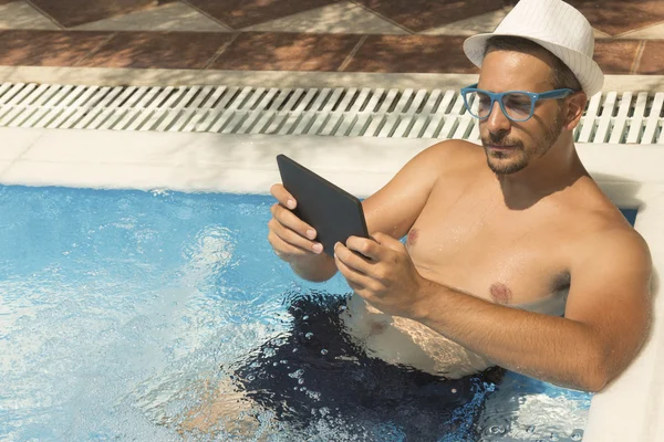 Young guy using tablet device while relaxing in the swimming pool