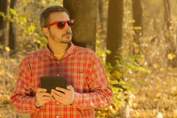 Man with a digital tablet leaning against the tree