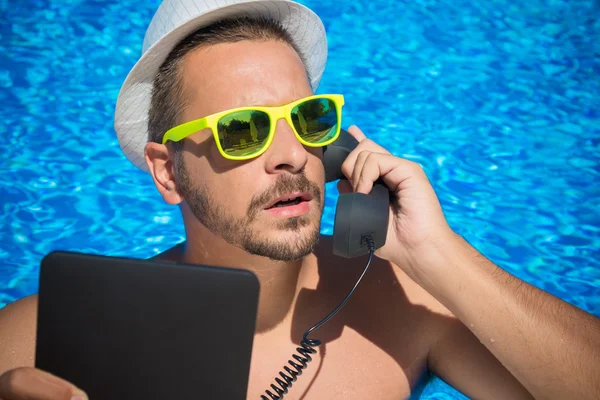 Young man using digital tablet and retro styled handset in the swimming pool.
