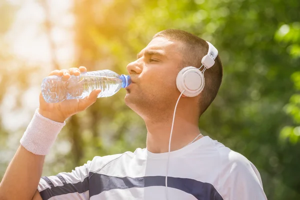 Sportsman with headphones drinking water from the plastic bottle outdoors