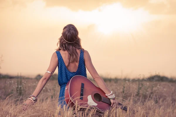 Young hippy woman with acoustic guitar enjoying the sunset