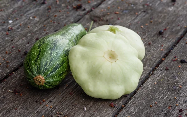 Zucchini and two pattypan squash harvested from the vegetable garden beds lie on the wooden table