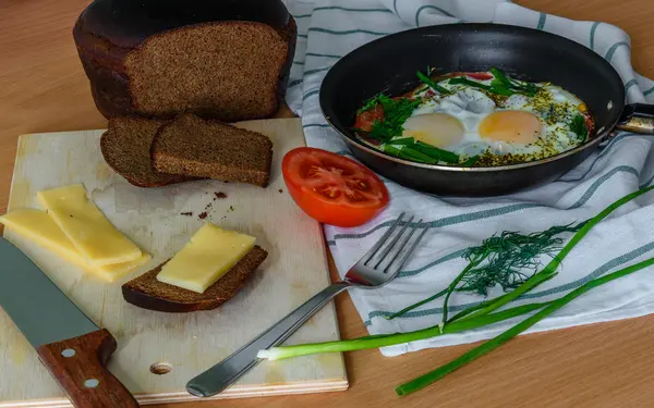 Fried eggs with herbs and tomatoes in a pan.