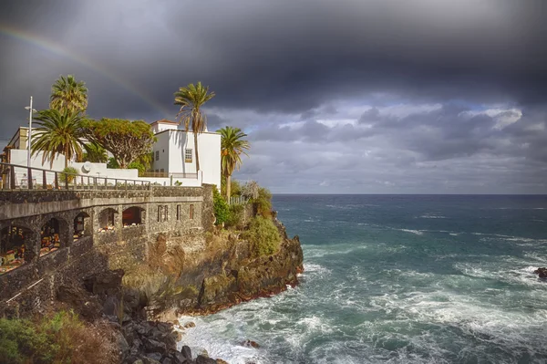 Town city hall over rocks and sea waves under a rainbow
