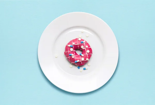 Creative concept photo of a donut covered with pills on a plate on blue background.