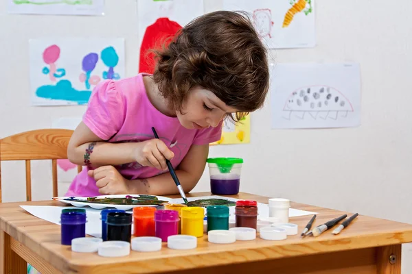 Little girl is drawing with paints and paintbrush
