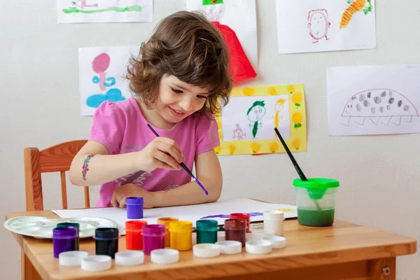 Little girl is drawing with paints and paintbrush