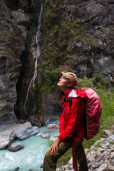 Portrait Young Pretty Girl Wearing Red Jacket Backpack Trail Mountains.Mountain Trekking Landscape WaterFall View Background.Woman Happy Smiling Close Rock River.Horizontal Photo.