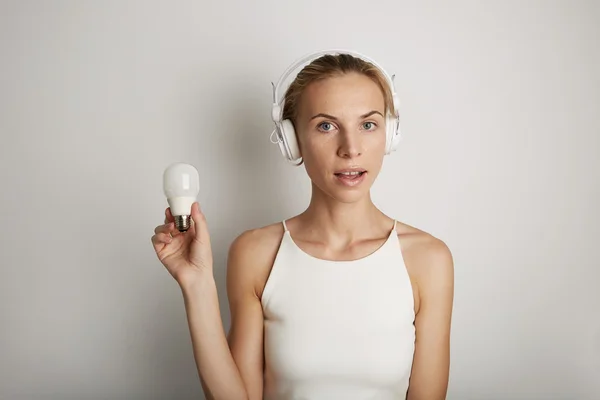 Portrait Handsome Young Woman Listening Music Player Headphones Blank White Background.Pretty Girl Looking Holding Energy Safe Bulb Hand Empty Wall.Beauty Lifestyle Fashion Hipster People Concept.