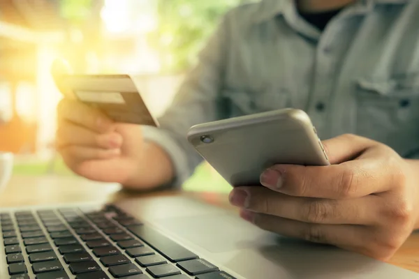 Online payment,Man\'s hands holding a credit card and using smart phone for online shopping with morning light. vintage filter effect.