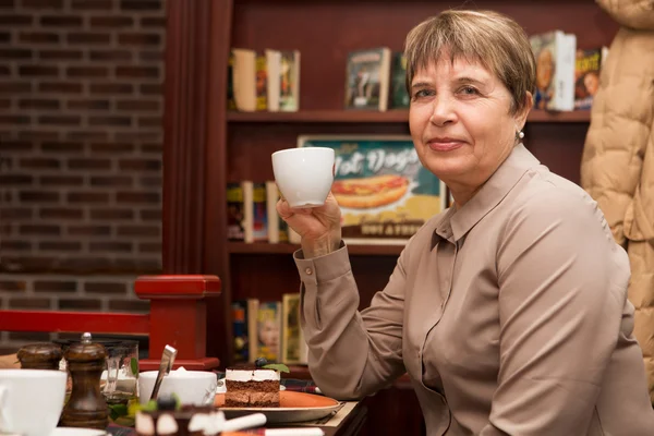 The portrait of the elderly woman in cafe with friends has tea