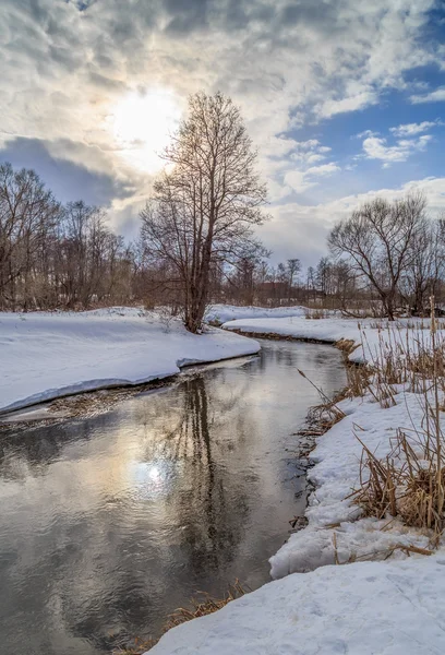 River, snow, sun through the clouds, on the banks of alder