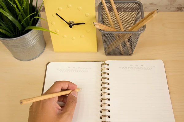 Man hand writing schedule job on the table with yellow clock