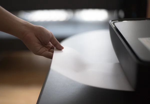 Person reaching hand and taking paper from printer on black leather tabl