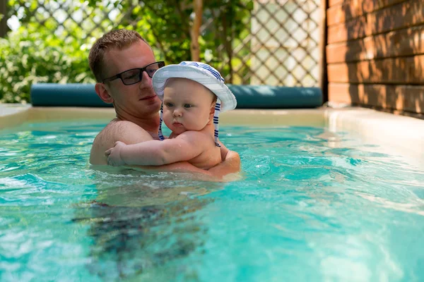 Father and small son in a panama hat swimming in the pool