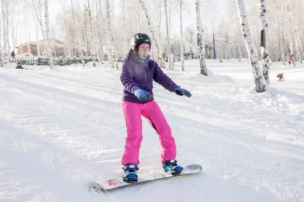 Girl in purple jacket and pink pants learn ride a snowboard
