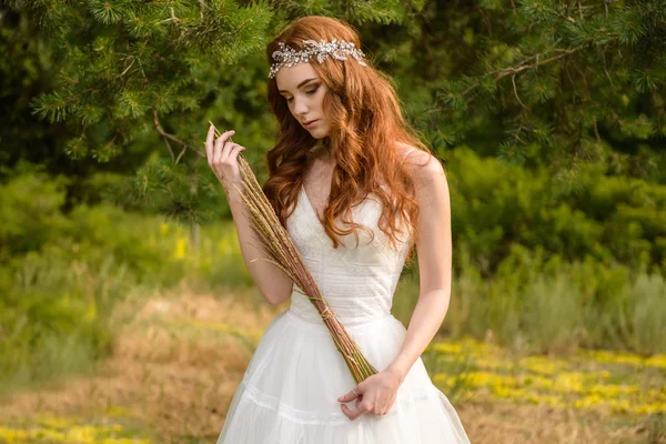 Redheaded young girl in the woods. Portrait of the bride in the Park. A girl holds wheat ears in the hands. hippie girl
