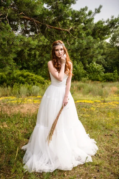 Redheaded young girl in the woods. Portrait of the bride in the Park. A girl holds wheat ears in the hands.