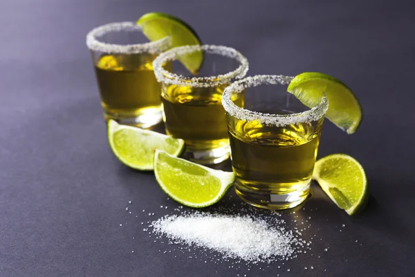 Gold tequila with lime and salt on dark table