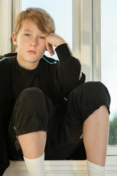 Depressed boy wearing black sweat suit by windows