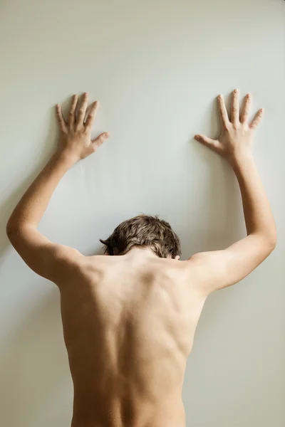 Vertical view on back of teen with hands on wall