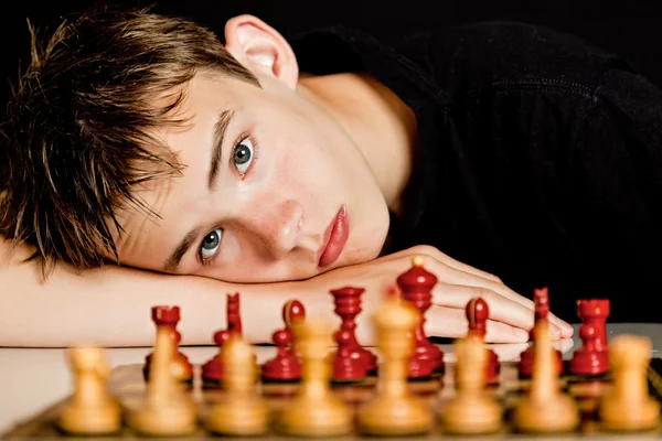 Teenage Boy Resting Head on Table Near Chess Board