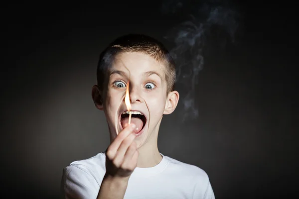 Frightened boy holding lit match in darkened room