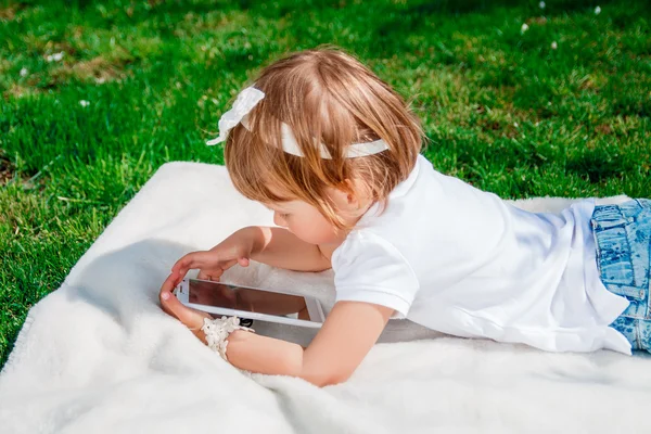 Little baby girl dressed in white polo and jeans.Girl Using a Tablet. Little girl studies with the tablet