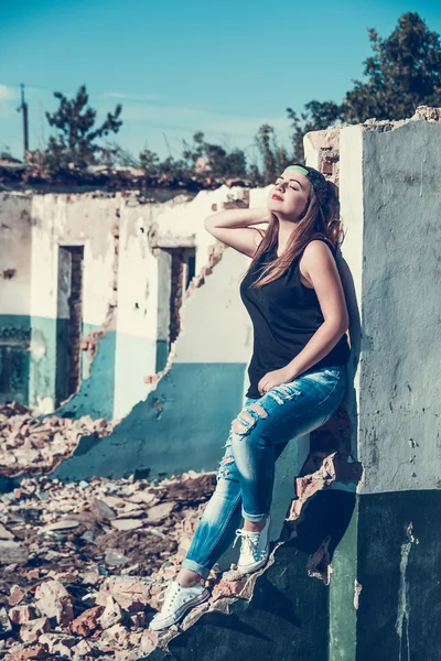 Attractive woman in jean and cup outfit posing in old ruined factory house