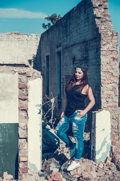 Attractive woman in jean and cup outfit posing in old ruined factory house