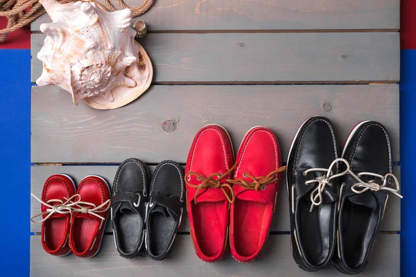 Family boat shoes on wooden background. Four pair of red and black    grey desk with rope  shell. Top view, copy space.  concept
