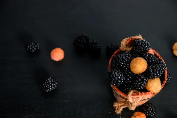 Black and yellow raspberries in a wooden basket on   background. Frame. Copy space. Top view.