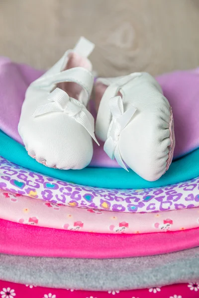 Folded pink and white bodysuit with shoes on it  grey wooden background. diaper for newborn girl. Stack of infant clothing. Child outfit. Close up.