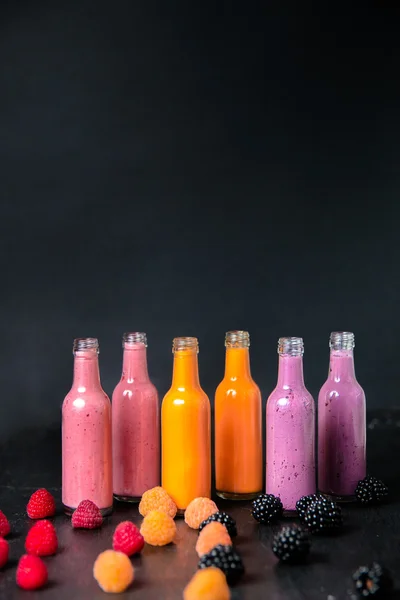 Six bottles with smoothies and raspberry, red, yellow, blackberry on black background. Milk shake in glass jar berries. diet or vegan food concept, fresh vitamin