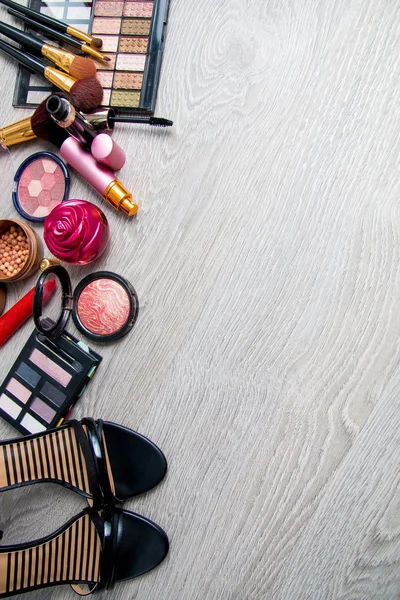 Set of decorative cosmetics and brushes near black heeled sandals on grey wooden background. Various makeup products. Top view, frame. Copy space.