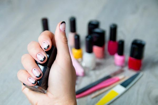 Black nail polish in female hand with tools for manicure and pedicure background. Close up.