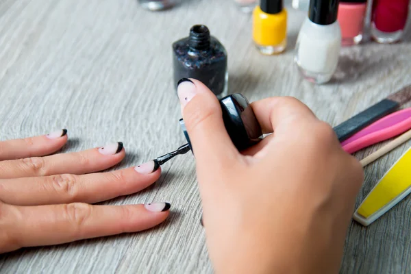Black nail polish being applied to hand with tools for manicure on background. Beautiful  process. Close up.