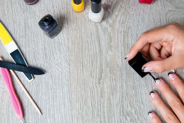 Black nail polish being applied to hand with tools for manicure on background. Beautiful  process.  Top view. Copy space. Frame.