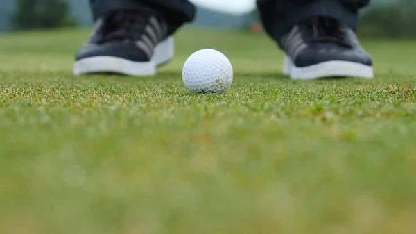 Golf player putting ball into hole, only feet and iron to be seen